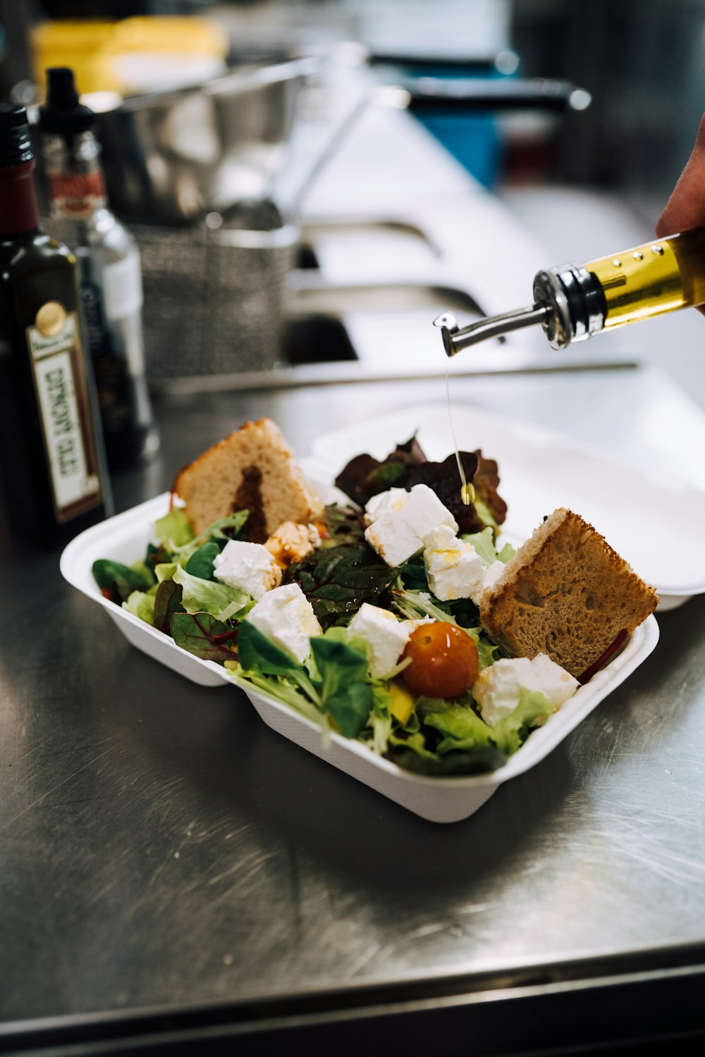 olive oil poured into green vegetable salad with cheese and croutons