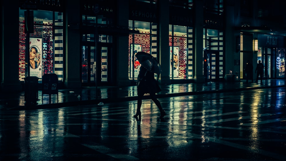 person with umbrella walking beside building during nighttime