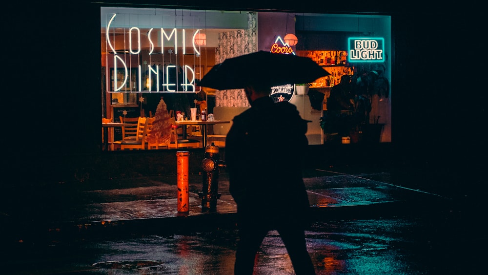 man under umbrella walking toward COsmic Diner building
