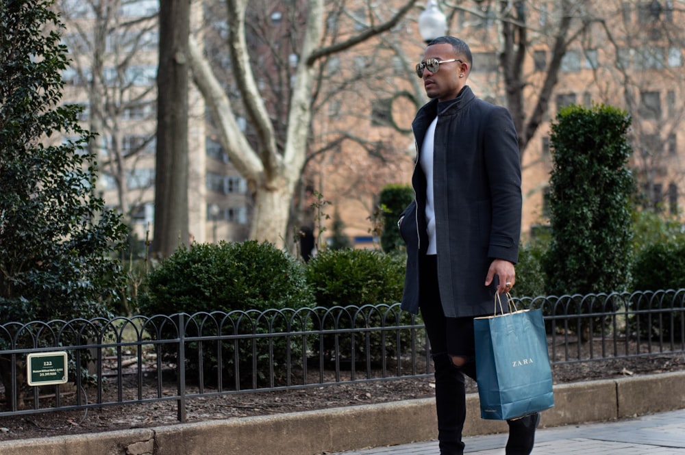 man wearing black jacket holding paper bag walking on road during daytime