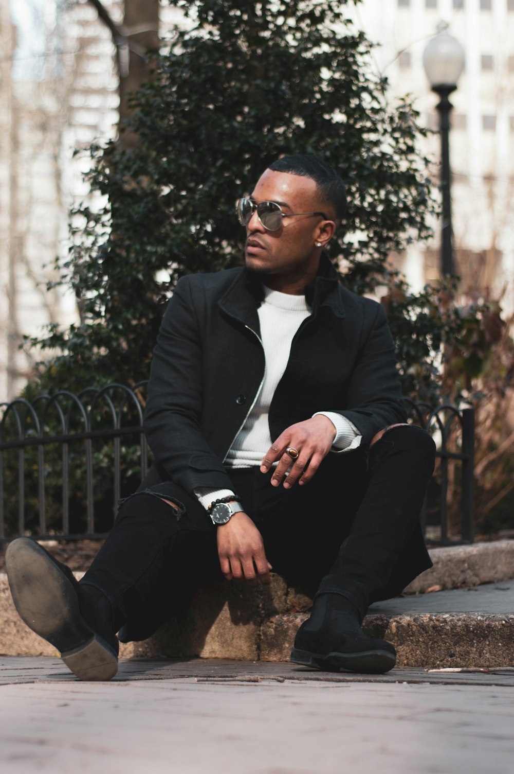 man in black coat sitting on sidewalk