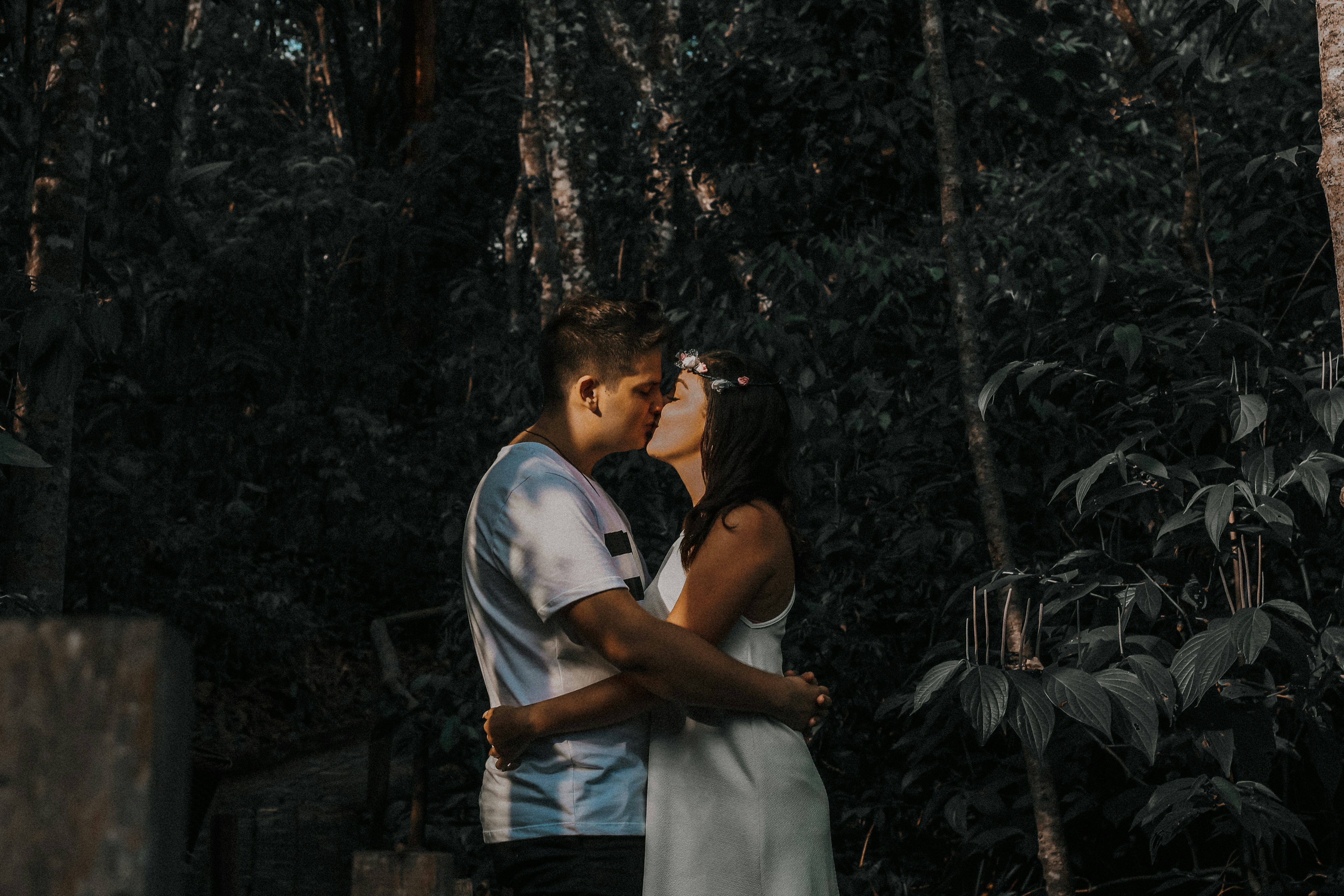 casal se beijando ao lado de plantas e árvores durante o dia