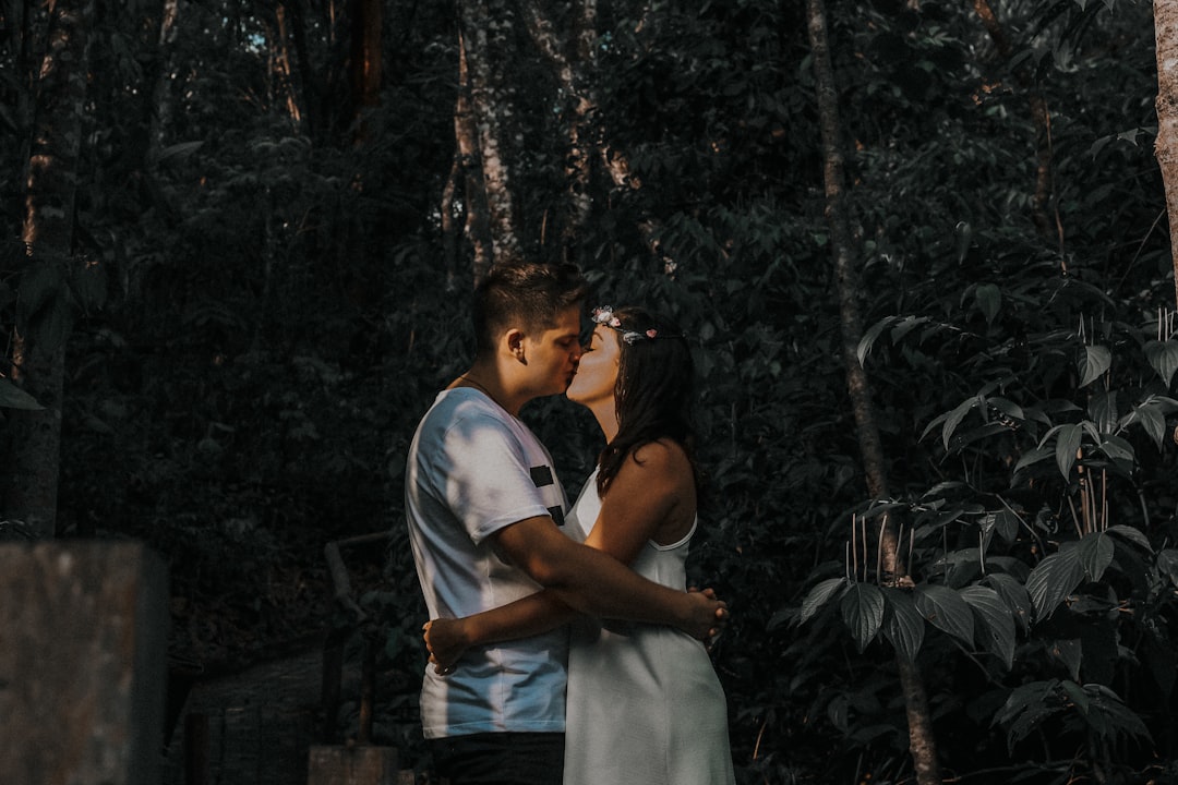 couple kissing beside plant and trees during daytime