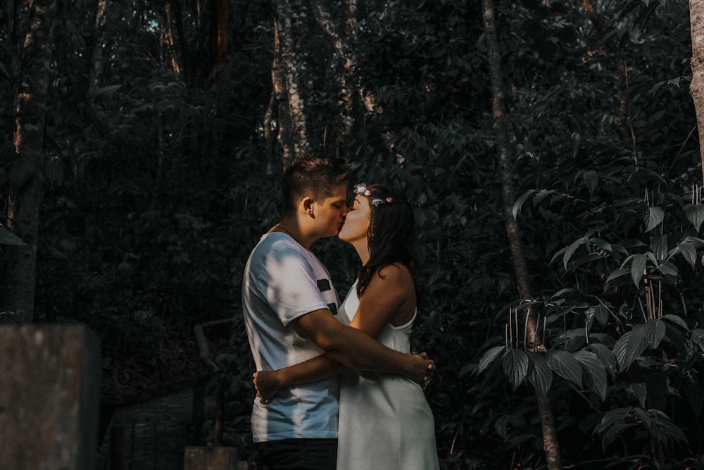 couple kissing beside plant and trees during daytime