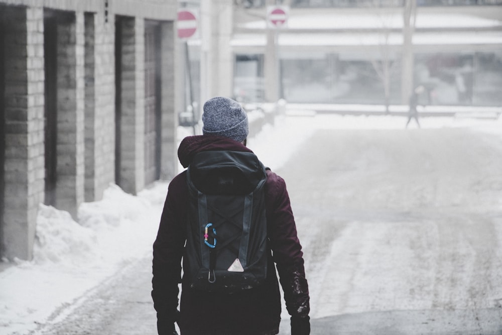 Hombre con sudadera con capucha negra y gorro gris caminando por un camino cubierto de nieve