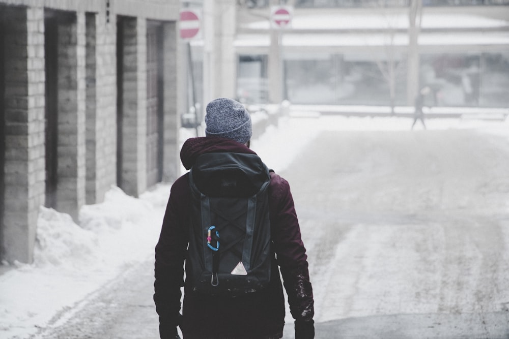 man wearing black hoodie and grey beanie walking on snow covered road
