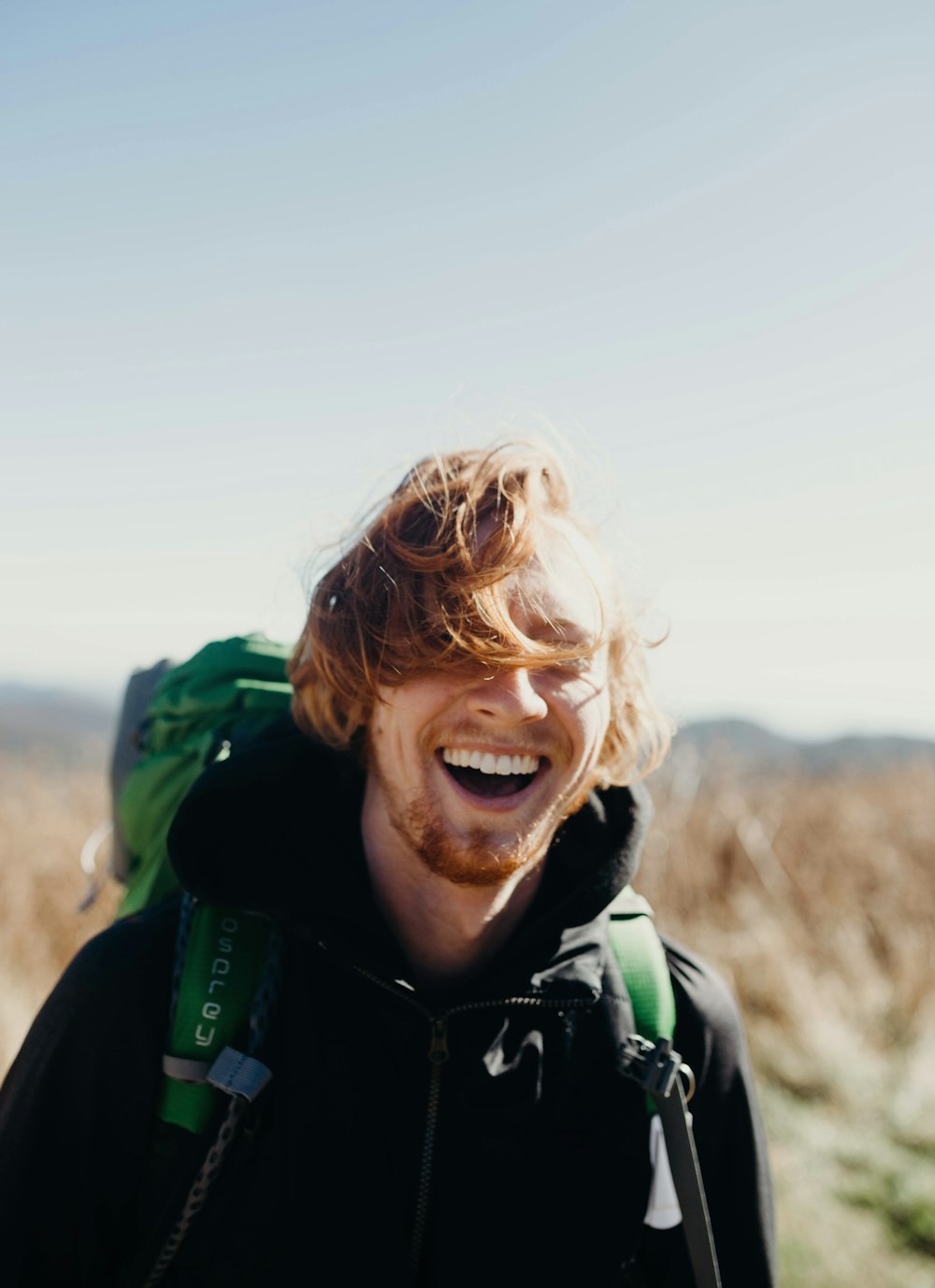 Hombre sonriente con bolsa verde de montañismo durante el día