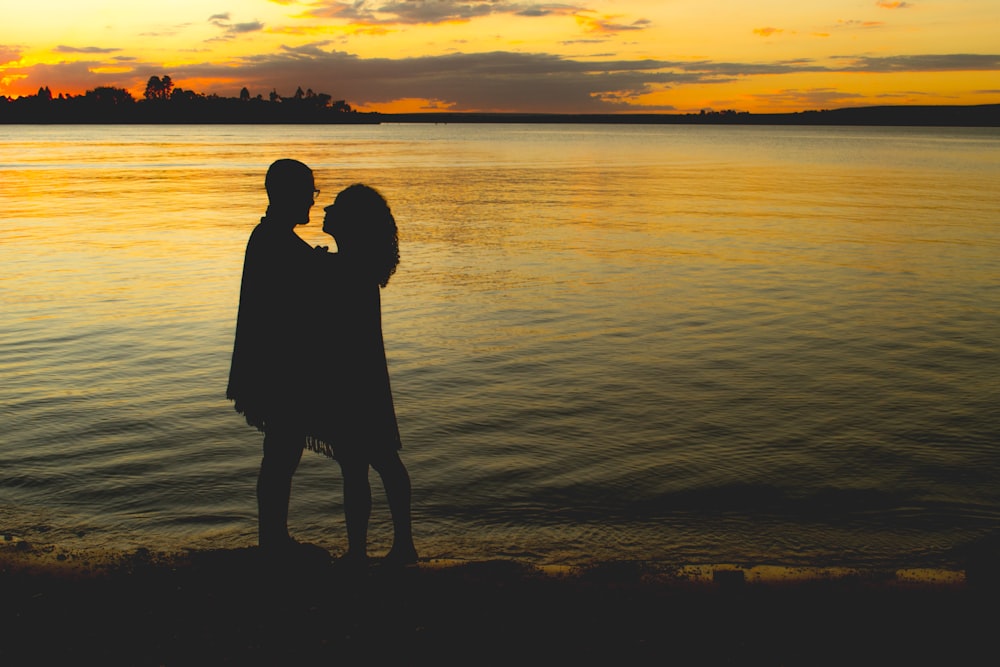 silhouette of couple on seashore under yellow sky