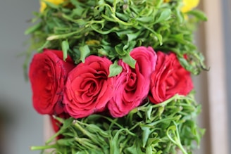 A close-up of a luxurious floral arrangement with deep red roses and dark greenery on a black tablecloth.