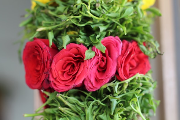 A close-up of a luxurious floral arrangement with deep red roses and dark greenery on a black tablecloth.