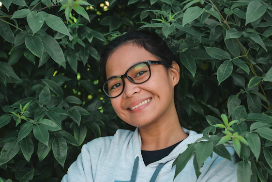 A smiling person taking a deep breath outdoors, surrounded by fresh green trees.