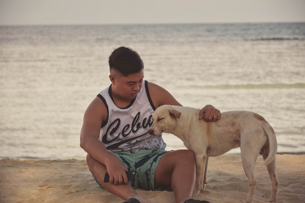 man sitting on shore beside white dog