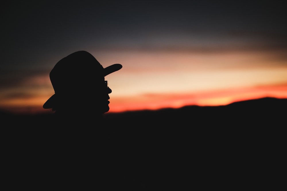 silhouette of person wearing hat and glasses during sunset