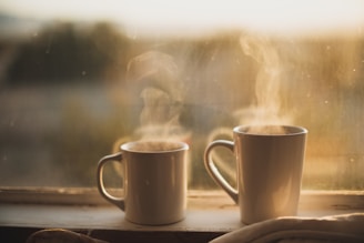A quiet evening photo of two mugs on a windowsill with city lights twinkling outside.