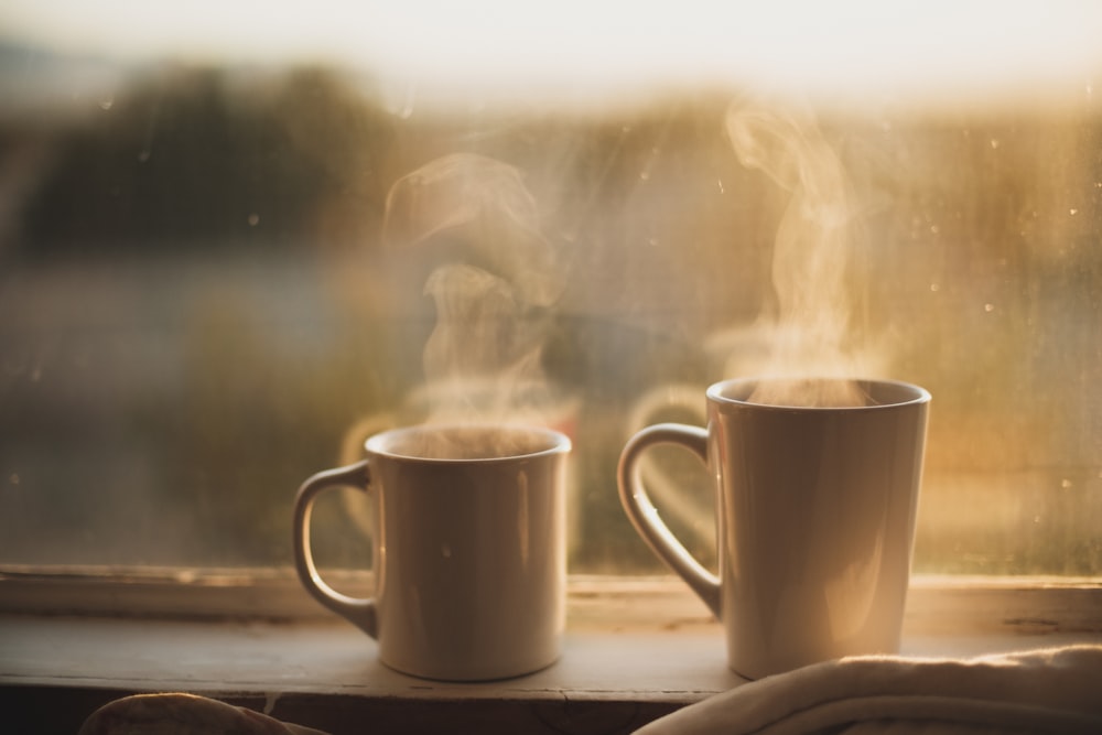 two white ceramic mugs near window