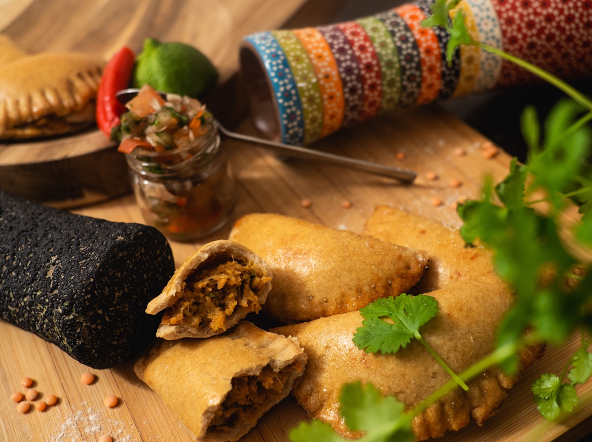 Golden baked empanadas served with chimichurri sauce on rustic wooden board