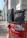 Two black bags are placed on top of a red India Post mailbox. The mailbox displays text in both English and Hindi, indicating sections for letters and packets. The background shows a curved building with white pillars, suggesting an urban setting.