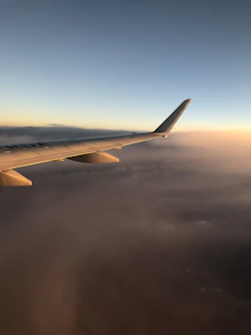 A scenic view of a plane soaring above fluffy white clouds at sunset.