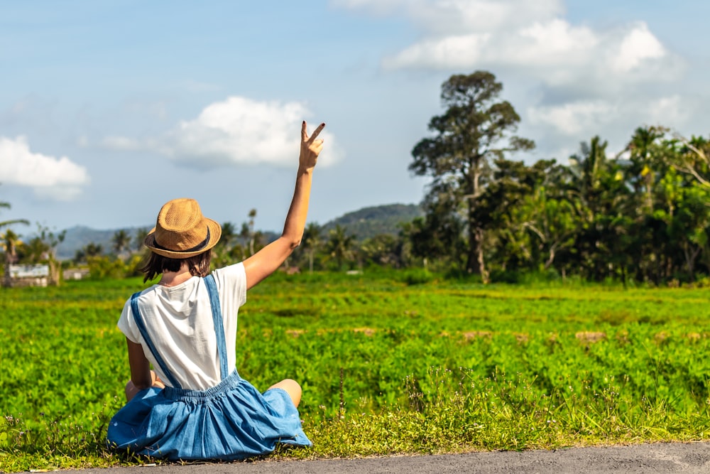 woman sitting on green grass while making peace sign post