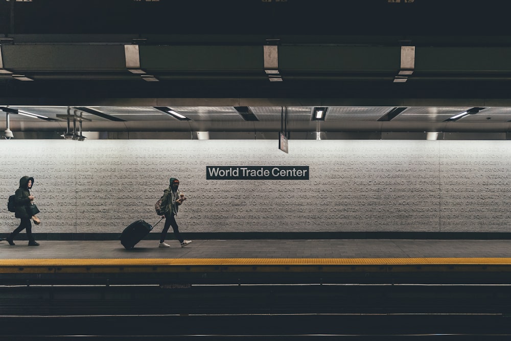 persona con bolsa rodante caminando por el costado de la barandilla con letreros del World Trade Center