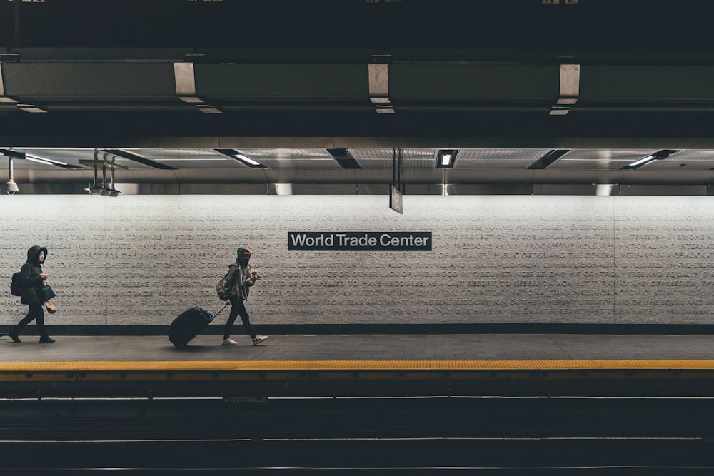 person with rolling bag walking on the side of the rail with World Trade Center signage