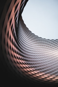 An architectural structure featuring a dynamic spiral pattern made of interwoven materials, creating a sense of depth. This design leads the eye towards the open sky visible through the circular opening at the top.