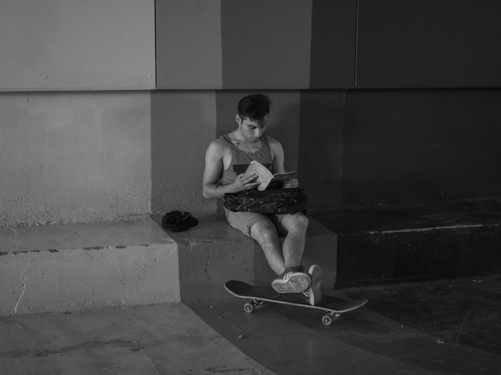 grayscale photography of man reading a book while feet's on skateboard