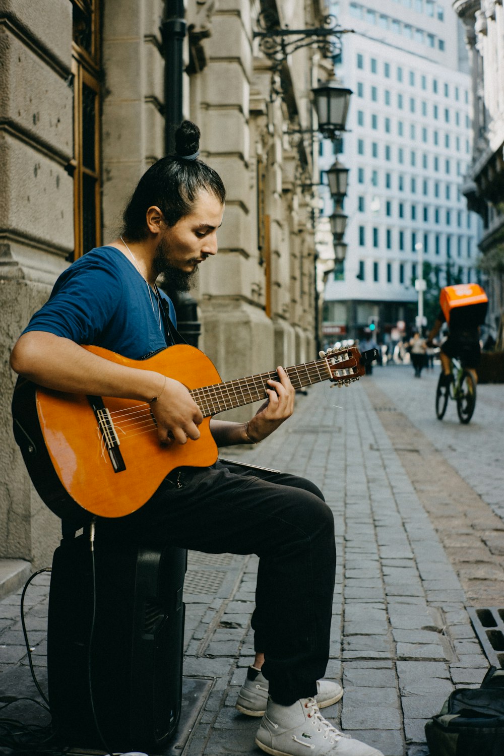 man playing guitar beside brown building