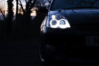 Bright car headlights shining on a dark road at dusk.