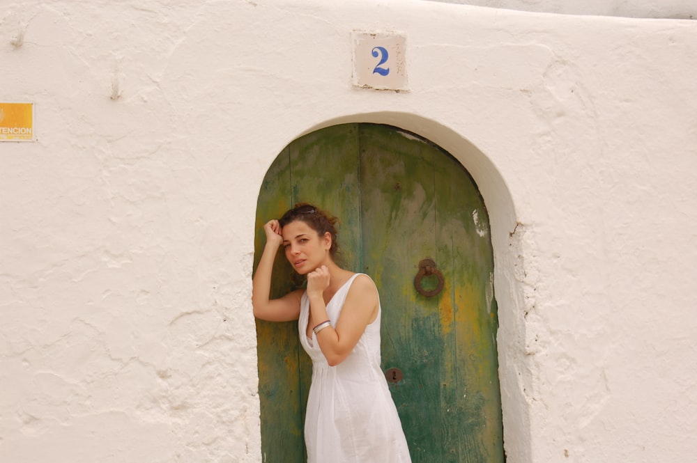 woman in white dress leaning on green and blue door during daytime ]