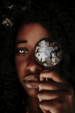 Close-up of a detective’s hands holding a magnifying glass over evidence photos.