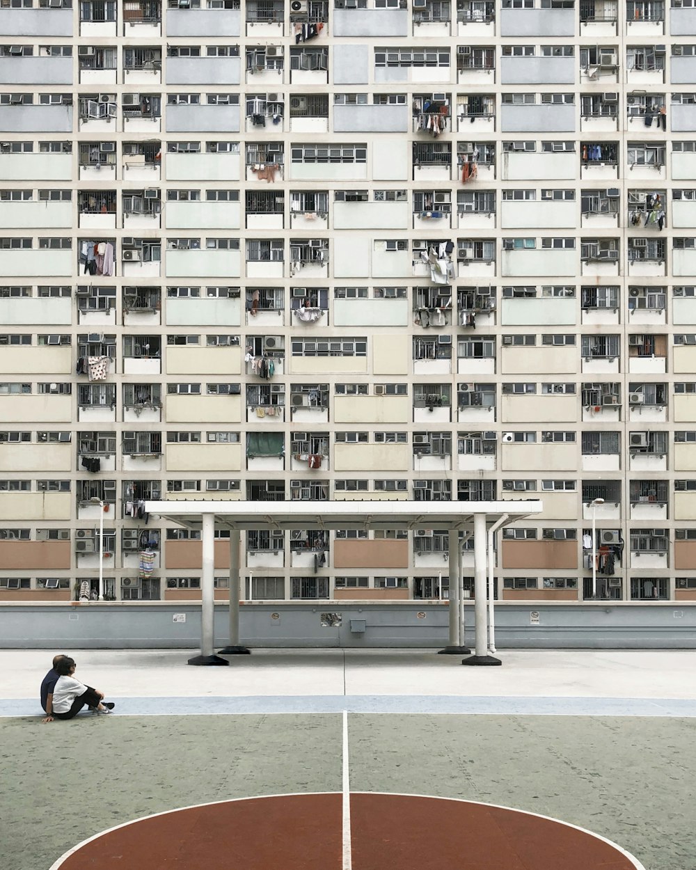 two people sitting on concrete pavement in front of high-rise building