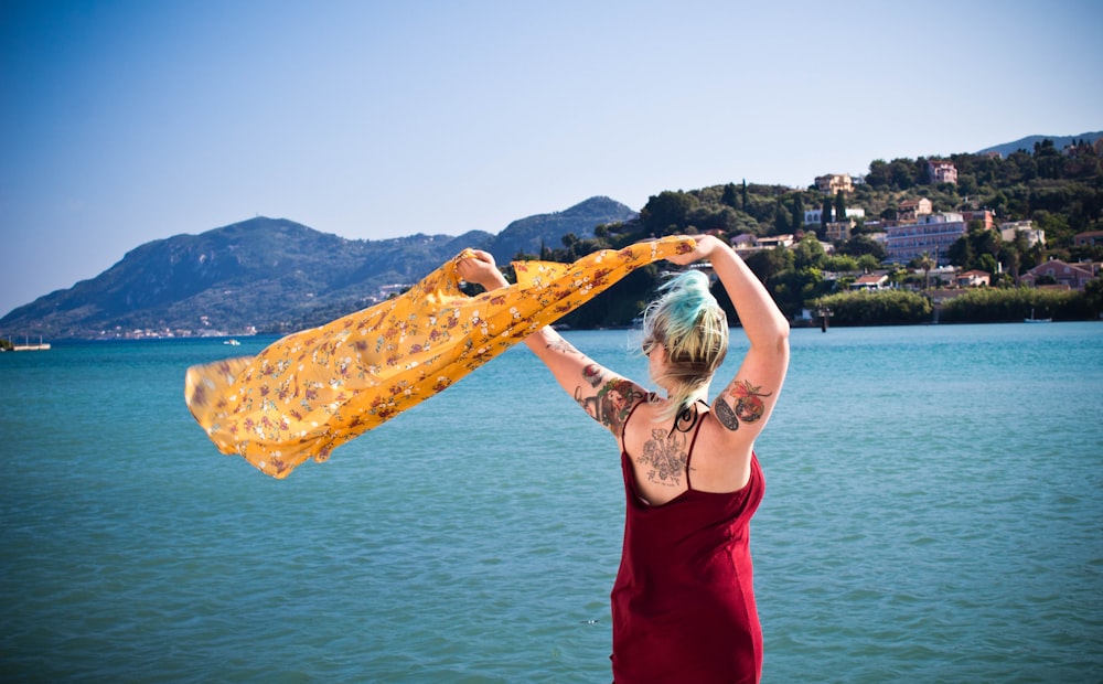 woman waving yellow textile near body of water during daytime