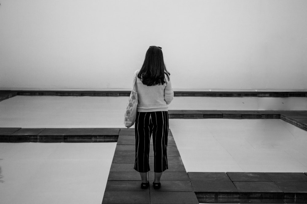 fotografia in scala di grigi di una donna in piedi accanto allo specchio d'acqua