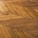 A detailed view of a wooden floor with a geometric chevron pattern. The wood planks are arranged in a herringbone style, showcasing various shades and textures of brown.
