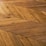A detailed view of a wooden floor with a geometric chevron pattern. The wood planks are arranged in a herringbone style, showcasing various shades and textures of brown.
