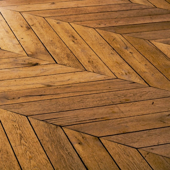 Close-up of elegant herringbone parquet floor in warm oak tones inside a cozy living room.