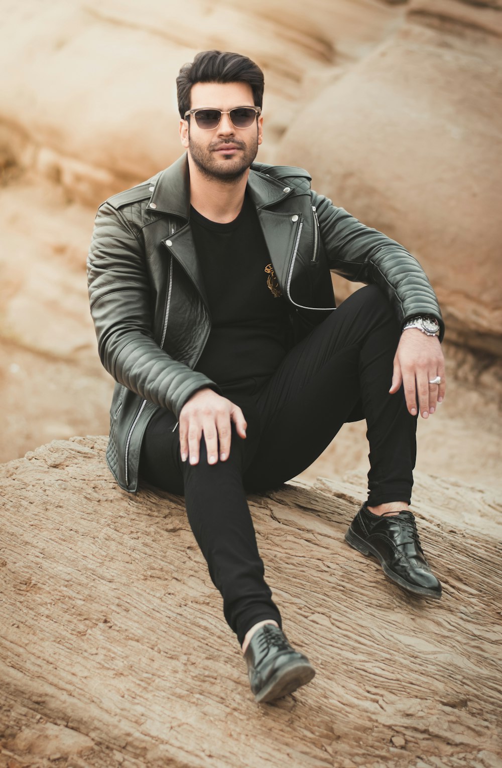 man sitting on rock with black leather jacket during daytime
