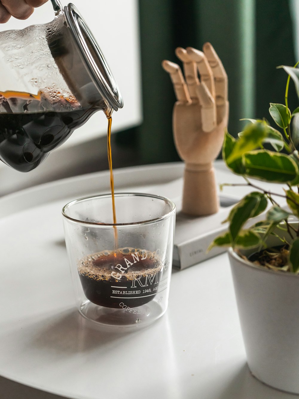 Selektives Fokusfoto einer Person, die Kaffee auf klares Trinkglas gießt