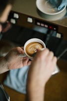 A smiling person holding a freshly brewed cup of coffee next to a compact espresso machine.