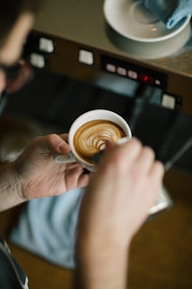 A smiling person holding a freshly brewed cup of coffee next to a compact espresso machine.