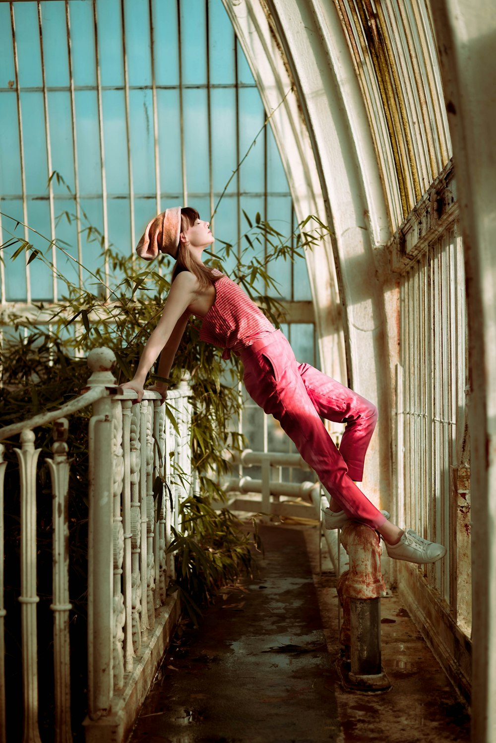 woman wearing pink overalls with feet on white pedestal while her hands holding on metal rail
