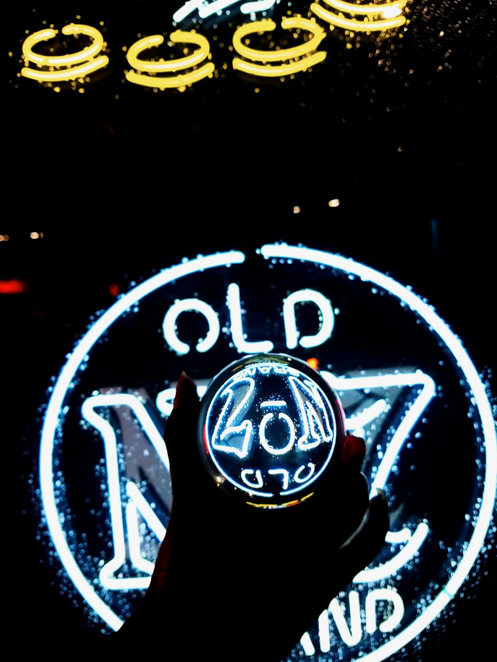 person holding drinking glass above Old no.7 neon light