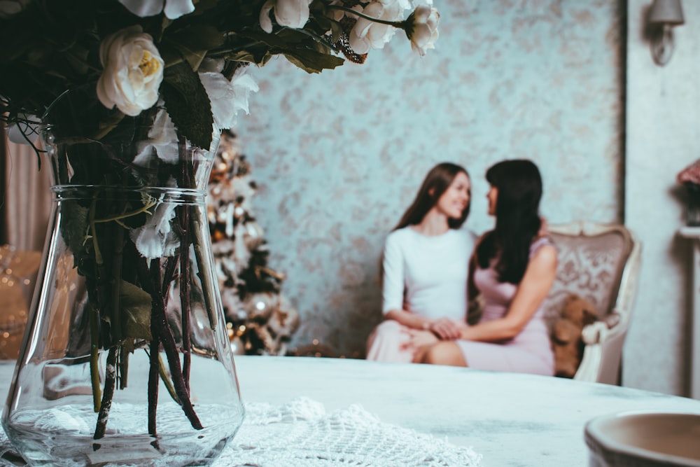 2 woman sitting on loveseatnear table with rose in vase