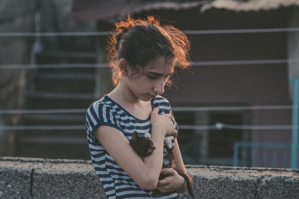 Foto de enfoque selectivo de mujer sosteniendo cachorro cerca de la pared gris