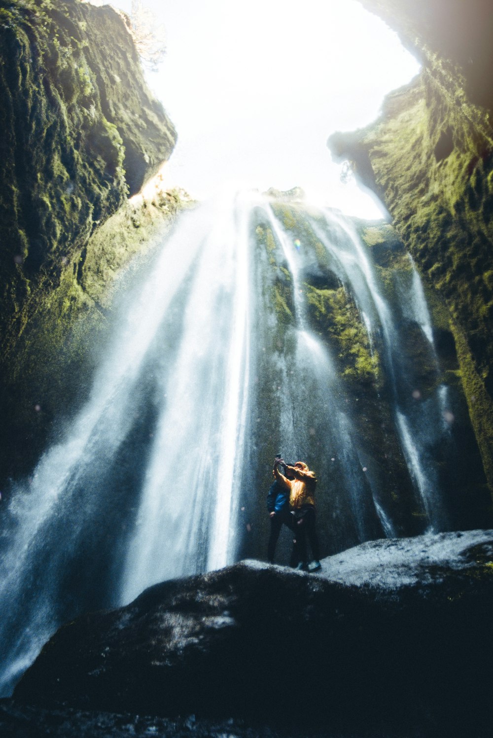 due persone in piedi sulla roccia con sfondo a cascata