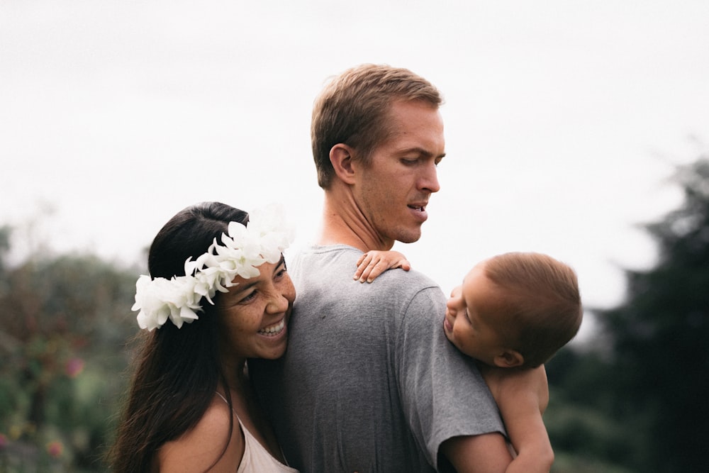 homme tenant le bébé et la femme à l’arrière souriant pendant la journée