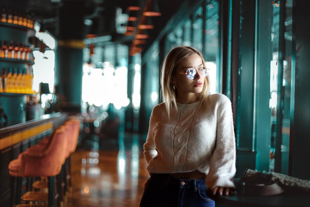 woman wearing white knit sweater standing beside wall