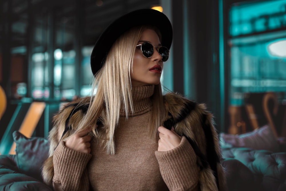 Femme portant un pull à col roulé marron, un chapeau noir et des lunettes de soleil noires