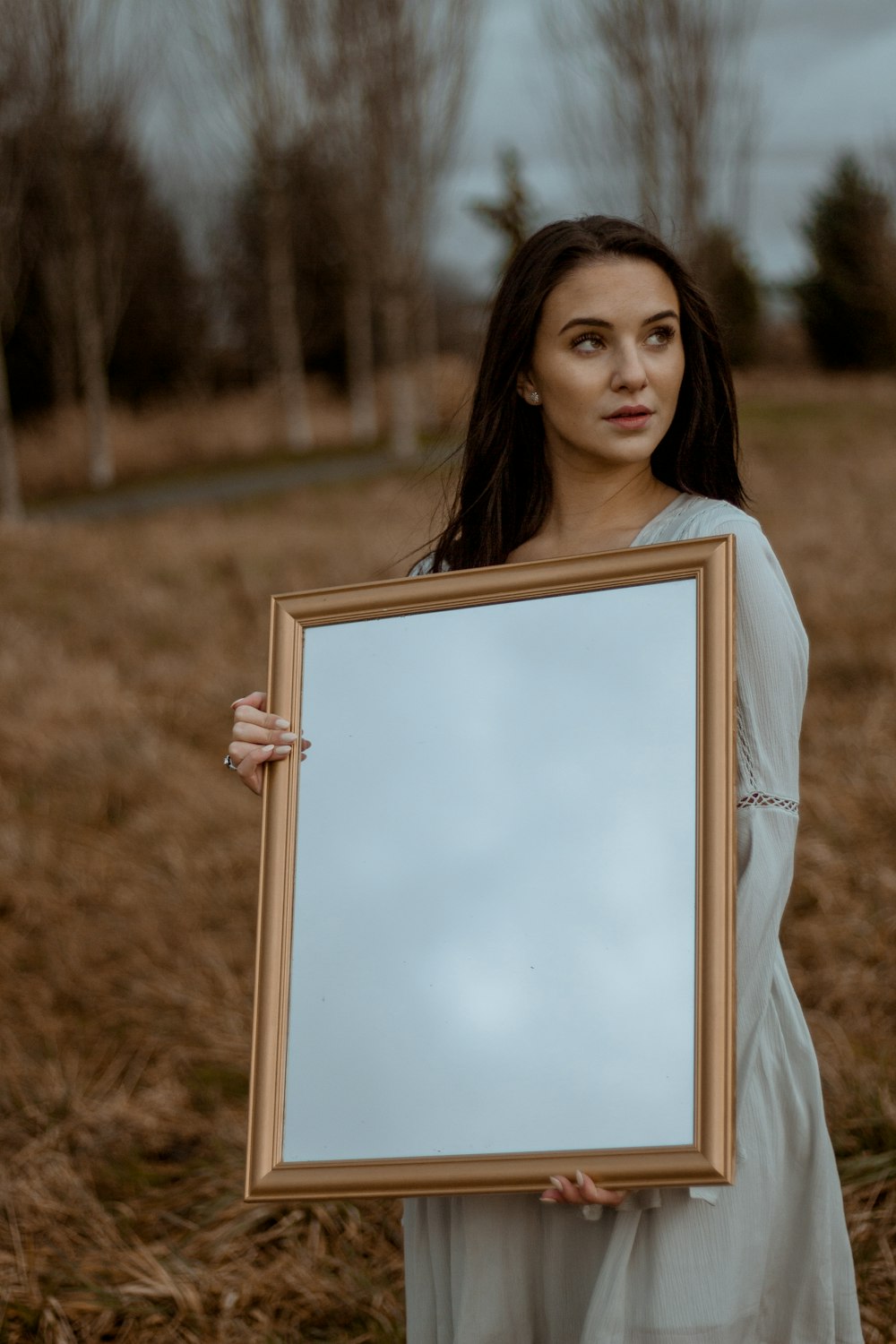woman in white dress standing on grass field while holding photo frame